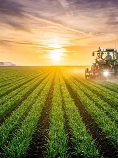 Sunrise over a vast agricultural field, a tractor cultivates the land under a colorful sky, representing modern farming and the future of agriculture.